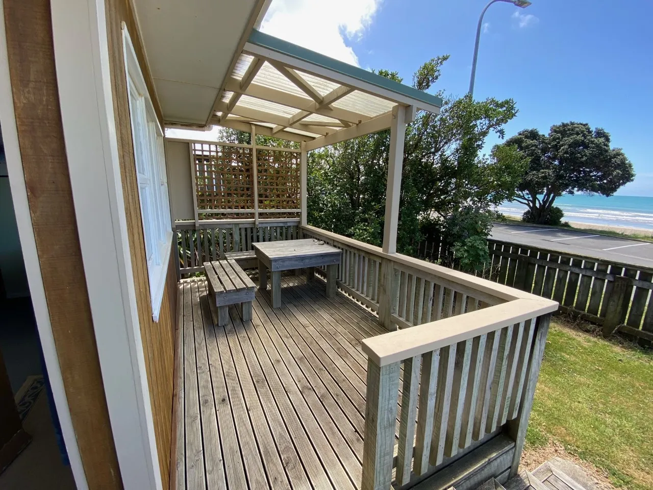 The covered timber deck at Bach B, with outdoor seating and a view of the sea