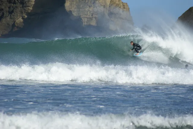 A surfer riding a green wave at the Gap, Castlepoint, with cliffs behind